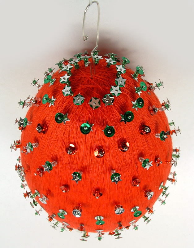 Top view of red thread wrapped ornament with sequins and pins.